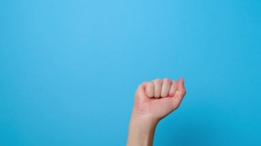 Tanımlanamayan genç bir kadının kapısına yumruğunu kaldırmış, reklam için fotokopi çekilen mavi stüdyo arka planında soyutlanmış. El hareketi. Uyarı işareti.