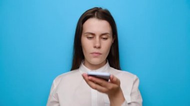 Elinde telefon tutan genç bir kadın akıllı telefondan sanal ses asistanını aktif hale getiriyor, kız sesli mesaj kaydediyor, arkadaşlarıyla online veya hoparlörden sohbet ediyor, mavi stüdyo arka planında izole edilmiş.