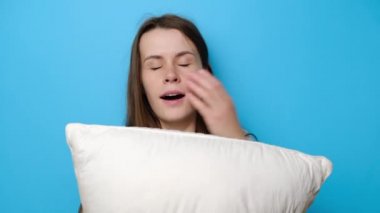 Uykulu, yorgun, beyaz, beyaz bir kadının portresi eliyle ağzını kapatır, esmer kız uyuduktan sonra esner, beyaz yastığı kucaklar, mavi stüdyo arka planında soyutlanır.