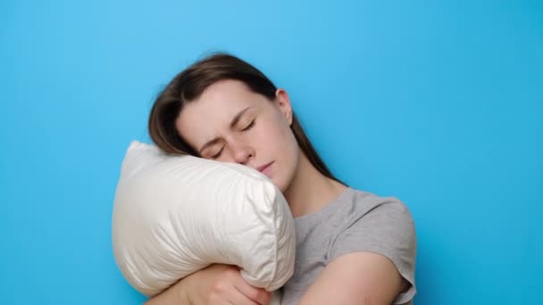 疲れた若い女性は 夜の睡眠後に首に痛みを感じる枕を包含します 目覚め痛みを伴う突然の痛みや剛性を持っています 睡眠中に誤った姿勢 青のスタジオの背景に隔離 — ストック動画