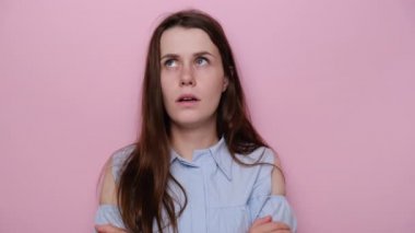 Üzgün genç kadın ellerini göğsünün üstüne koyuyor, üzgün bir şekilde kameraya bakıyor ve iç çekiyor. Memnuniyetsiz depresyondaki kız gücenmiş hissediyor, mavi gömlek giyiyor, pembe stüdyo arka planında soyutlanmış.