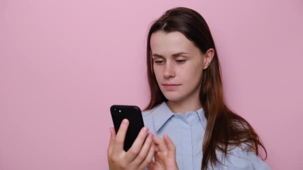 興奮した若い可愛い女の子のクローズアップ肖像は 携帯電話でSms勝利通知を受けました ピンクのスタジオの壁に隔離され 成功を祝う 良いニュースでメッセージを読むユーフォリックミレニアル女性 — ストック動画