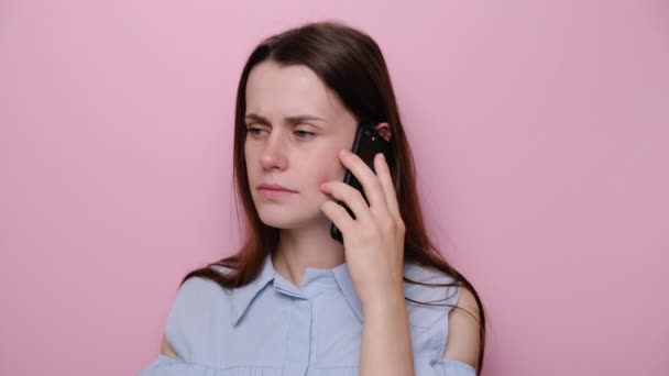 スタジオのピンクの壁の背景に隔離された青いシャツを着て スマートフォンで話して怒っている若い白人女性の肖像画を閉じます ライフスタイル 感情やストレスの概念 — ストック動画