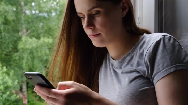 Χαρούμενη Νεαρή Γυναίκα Κάθεται Στο Περβάζι Κρατώντας Smartphone Χρησιμοποιώντας Mobile — Αρχείο Βίντεο