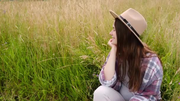 Şapkalı Yeşil Çimenlerde Oturan Elini Çenesinde Tutan Kameraya Mutlu Samimi — Stok video