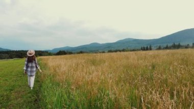 Şapkalı neşeli genç bir kadın arka plandaki dağlarda yürür, güzel yaz manzaralarından hoşlanır. Romantik, hayalperest ve ilham verici bir yürüyüş. Gerçek vahşi yaşam tarzını keşfet.