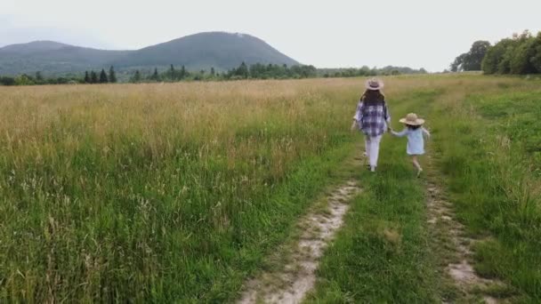 无人机跟随年轻的母亲和可爱的女儿 快乐的家人在田边的路上奔跑 把帽子抛向空中 梦幻般的家庭走过游手好闲的探险家和自然环境中的自由情人 — 图库视频影像