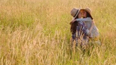 Samimi bir anaokulu kızı neşeli, genç bir anneye sarılıyor. Şapkalı mutlu anne, çimlerin üzerinde oturan küçük kıza minnettar. Samimi duyguların ve açık havada eğlencenin dışında.