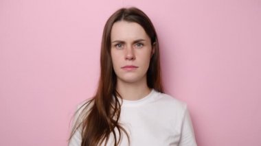 Umutsuz, sinirli genç bir kadının portresi megafonla el hareketleriyle bağırıyor, tüm nefret saldırganlığını ifade ediyor, yüksek sesle bağırıyor, beyaz tişört giyiyor, pembe stüdyo arka planında izole edilmiş.