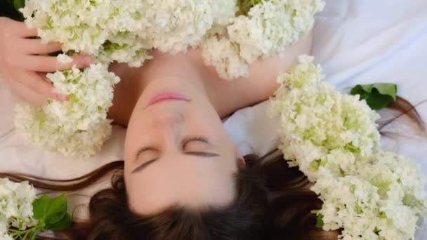 迷人的黑发女人躺在新鲜白花旁舒适的白色床上的浪漫特写 俯瞰可爱而沉稳迷人的小女孩散发着淡淡的季节鲜花的芬芳 慢动作 — 图库视频影像