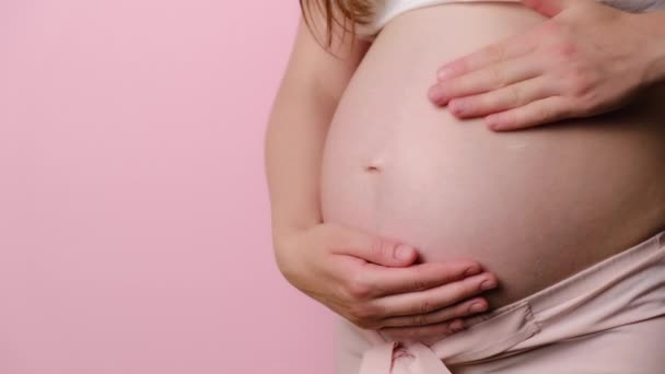 妊娠中の女性の閉鎖は ストレッチマークを防止するために妊娠中の腹にスキンケアクリームを適用します コピースペースとピンクのスタジオの背景に隔離されました 妊娠中 — ストック動画