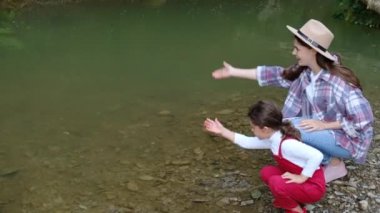 Şapkalı mutlu bir anne ve neşe içinde sıçrayan küçük bir kız yaz tatilinin tadını çıkarıyor. Nehir kenarında yaz tatilini kutluyor. Şefkat kavramı, macera, aile bağları bakım ve koruma