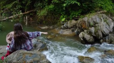 Genç esmer anne ve şapkalı şirin anaokulu kızı, şelalenin yaban nehrinin kenarında otururken, yeni maceralar için ileriye bakarlar. Aile birlikte aktif yaz haftasonunun tadını çıkarır..