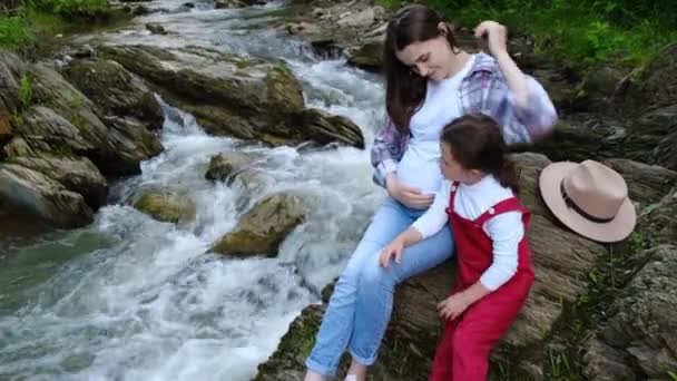 Вагітна Мати Сидить Своєю Маленькою Дошкільною Донькою Біля Струмка Води — стокове відео