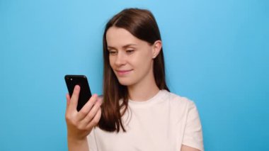 Genç bir kadın elinde modern telefon şakası videosuyla gülüyor, uzaktan sohbetin tadını çıkarıyor, mavi arka planda soyutlanmış. Boş zaman ve eğlence için internet eğlencesi modern aletler kullanımı kavramını kullanın
