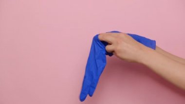 Tanınmayan bir kadın, pembe arka planda izole edilmiş koronavirüs salgını nedeniyle ellerine mavi koruyucu eldiven takıyor. Kovid-2019 salgın hastalığını önleyici önlemler. Virüs kavramını durdur