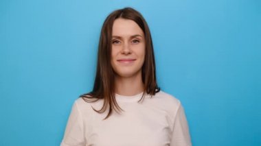 Geniş, büyüleyici gülümsemesi olan genç bir kız ellerini göğsüne koydu. Mavi stüdyo arka planında izole edilmiş, kalp şeklinde bir hayırseverlik sembolü ve insani nezaket. Cömertlik serbestlik işareti kavramı