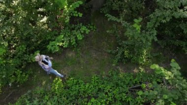 Karantina sonu, covid-19 yenilmiş konsept. Tıbbi steril maskeli, tatlı hamile bir kadının hava aracı görüntüsü ormanda yürüyor, koruyucu yüz maskesi çıkartıyor, gülümsüyor derin mutlu ve sağlıklı nefes alıyor.