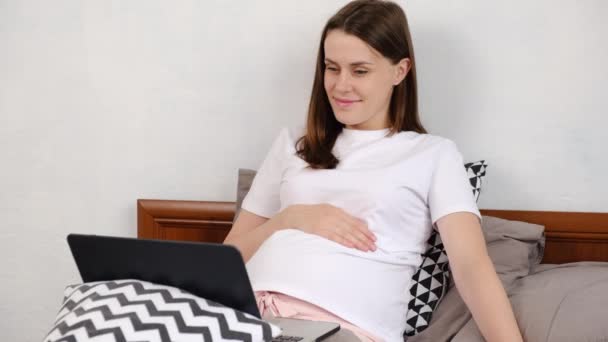 快乐的年轻孕妇看着屏幕笔记本电脑 躺在客厅舒适的床上 漂亮的笑着未来的妈妈看滑稽视频 喜剧演员电影在家里 娱乐概念 — 图库视频影像