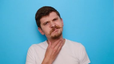 Hüzünlü bin yıllık adam ellerini boynunda tutuyor, yorgun genç adam boğularak ölüyor, boğazı ağrıyor, sinirleniyor, sağlıksız, yutması zor, mavi stüdyo arka planında izole edilmiş.