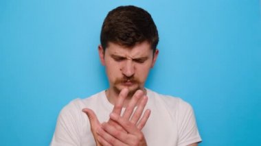 Mavi arka planda duran mutsuz milenyum adamı romatizma eklem iltihabından muzdarip el masajı yapan, bileğe dokunan adam eklem ağrısını hisseden, osteoartrit hastalığı olan bir adam.