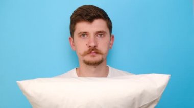 Kafkasyalı hoşnutsuz bir adam gücenmiş, suratını asmış, kötü bir uyku çekmiş, sinirli, gürültüden rahatsız olmuş, uykusuzluktan muzdarip, mavi stüdyo arka planında izole edilmiş,