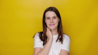 Sarı stüdyo arka planında kameraya bakarak gülümseyen hoş bir genç kadın. Çekici kız gülümsemesi, beyaz tişört giymesi, televizyon reklamı için kadın oyuncu seçimi, üniversite öğrencisi portresi konsepti.