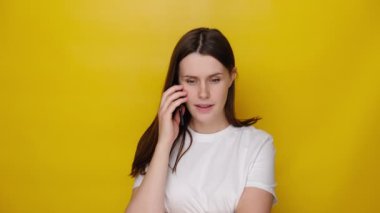 Endişeli kadın akıllı telefon çözme sorunları hakkında konuşuyor, endişeli kız cep telefonuyla konuşuyor zor bir konuşma yapıyor, sarı stüdyo arka planında izole edilmiş.