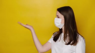 Genç bir kadın kendini koronavirüsten korumak için solunum maskesi takıyor. Promosyon metni için boş kopya alanı gösteriyor. Stüdyonun sarı arka planında izole edilmiş. Virüs salgını