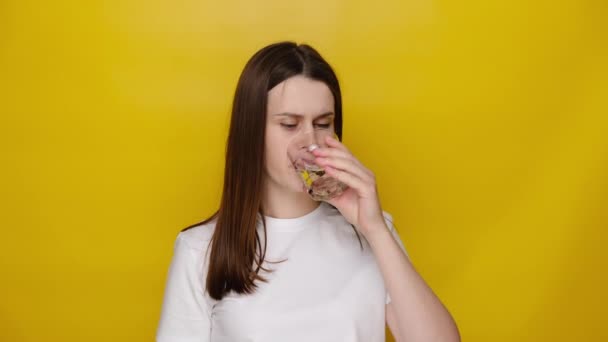 ブルネットの女性は氷の水を飲んで 突然ひどい歯痛 敏感な歯と空洞からの痛みを感じ コピースペースと黄色のスタジオの背景に隔離された 歯科問題の概念 — ストック動画