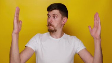 Şaşırmış genç adam elleriyle büyük bir jest yapıyor. Etkilenmiş adam geniş bir şey gösteriyor. Beyaz tişört giyiyor. İnsanların duygu kavramı
