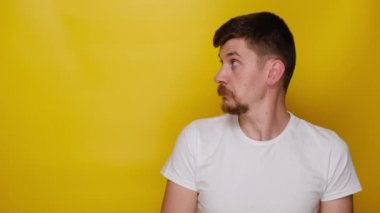 Hayret verici ifadesi olan mutlu genç bir adamın portresi reklamınız ya da tanıtım içeriğiniz için boş bir fotokopi alanı gösterir, beyaz tişört giyer, sarı stüdyo arka planında poz verir.