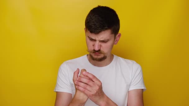 疲倦不健康的年轻人按摩疼痛的手 患有腕管综合症 身穿白色T恤 隔离在黄色的工作室背景 扭伤腕部 肌肉僵硬 — 图库视频影像