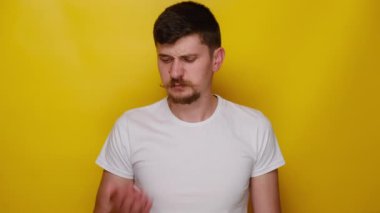 Sinirli genç adamın portresi nefesini kontrol ediyor, kötü bir koku alıyor, burnunu çimdikliyor, beyaz tişört giyiyor, sarı stüdyo arka planında kopya alanı olan izole edilmiş. Kötü koku konsepti