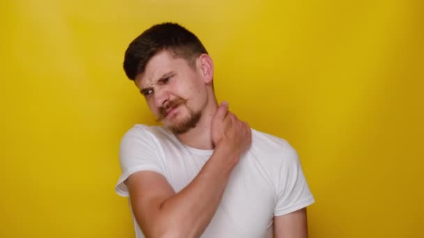 疲れ若い男は 関節の肩の痛みを緩和するために 白いTシャツを着て 黄色のスタジオの背景に隔離された緊張した筋肉をこすり疲労硬い首を傷つけるマッサージ 線維筋痛症の概念 — ストック動画