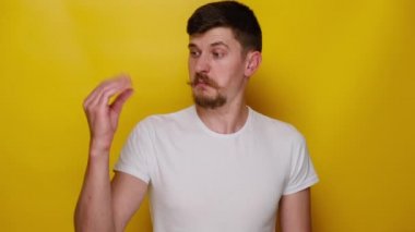 Canı sıkkın genç adamın anlamsız jestler yapan, dedikoducu umursamaz, beyaz tişörtlü, sarı arka planda soyutlanmış portresi. Sinirli adam bla-bla hareketi yapıyor.