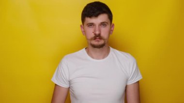 Tehlikeden kaçınmak için tavsiye veren, beyaz tişört giyen, onaylanmayan, sarı arka planda izole edilmiş, ciddi bir genç adam uyarısı..