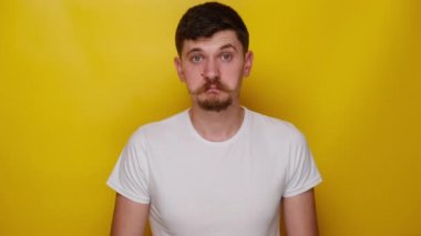 Kararsız genç adam ellerini yana atıyor, omuz silkiyor, soruya cevap veremiyor, beyaz tişört giyiyor, hiçbir fikri yok, sarı stüdyo arka planında izole edilmiş. insanlar duygu kavramı
