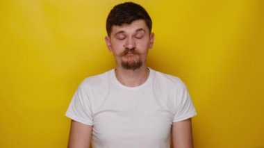 Suratı asık üzgün bir adam, kameraya doğru mutsuz görünüyor. Sıkılmış genç bir adam, motivasyon eksikliği, ilgisizlik, tişört giyiyor, sarı arka planda izole edilmiş. İnsan duyguları