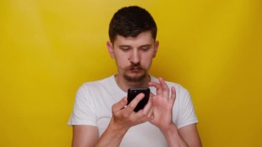 Sarı stüdyo arka planında izole edilmiş genç adam elinde telefonla konuşuyor akıllı telefondan sanal dijital ses asistanını etkinleştiriyor, sesli mesaj kaydediyor, arkadaşlarıyla online veya hoparlörden konuşuyor..
