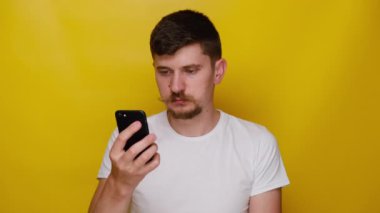 Sinirli genç adam huysuz kız arkadaşıyla konuşuyor, cep telefonu kullanıyor, beyaz tişört giyiyor, sarı stüdyo arka planında fotokopi alanı ile izole edilmiş. İnsanlar samimi duygular yaşam tarzı konsepti