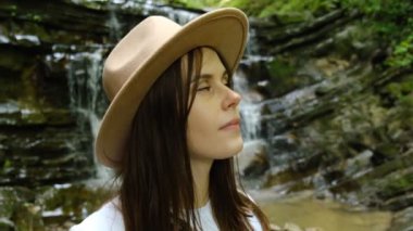 Sakin doğanın tadını çıkaran şapkalı çekici genç bir kadının yakın portresi. Hayalperest güzel kız yaz günü aktif bir hafta sonunun tadını çıkarıyor, temiz hava soluyor. Macera ve seyahat kavramı. Yavaş çekim