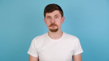 Elleriyle büyük boy jest yapan şaşırmış bir adam. Etkilenmiş genç bir adam tişört giymiş, mavi stüdyo arka planında kopya alanı olan geniş bir şey gösteriyor. İnsanların duygu kavramı