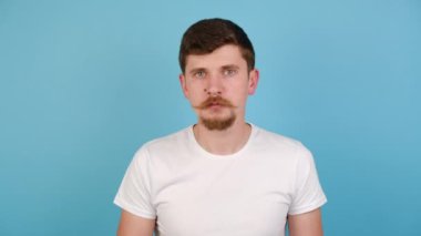 Ciddi genç adam kameraya bak gizli bilgileri söyle, sakallı adam hoparlörü paylaş özel satış promosyonu yap, beyaz tişört giy, mavi stüdyo arka planında kopya alanı olan izole edilmiş