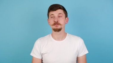 Genç adam güzel kokudan ya da hoş kokudan hoşlanıyor, sakin nefes alıyor, temiz hava alıyor, stres egzersizleri yapıyor, beyaz gömlek giyiyor, mavi stüdyo arka planında izole edilmiş barışçıl bir adam.