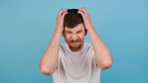 Unhappy Young Man Isolated Blue Studio Background Scratches Head Hands — Stock Video