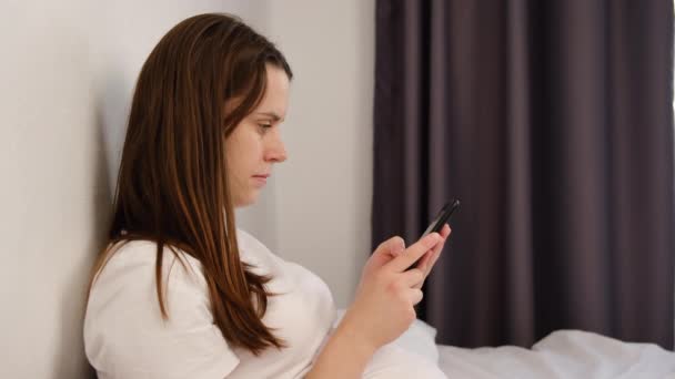 Boční pohled mladé ženy probudit ležící v posteli tráví čas používá smartphone, začíná nový den zkontrolovat sociální sítě zprávy, komunikace s přáteli, přehled plánu dne v kalendáři koncepce