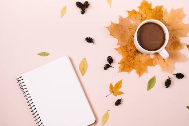 Düz kompozisyon, kuru akçaağaç yaprakları, defter ve pembe arka planda kahve fincanı. Yaratıcı sonbahar, şükran günü, sonbahar, cadılar bayramı konsepti. Üst görünüm, alanı kopyala
