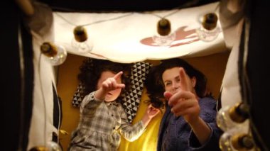 Neşeli anne ve tatlı kızın gölgeli balkabağı ve çelenk şeklinde dekorasyonlar arasında çadırda yan yana yatması. Aile, Coronavirus salgını sırasında Cadılar Bayramı 'nı evde kutlar.