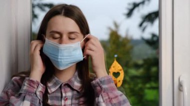Tıbbi maske takan genç bir kadın kalp şeklinde bir deliği olan sonbahar yaprağının yanındaki pervazda oturuyor. Bu sayede Covid-19 hastalığıyla mücadelede doktorlara ve hemşirelere şükranlarını sunuyor.